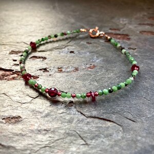 Op de afbeelding: Een delicate armband gemaakt met groene en rode edelsteen kralen. De armband heeft een gouden sluiting.