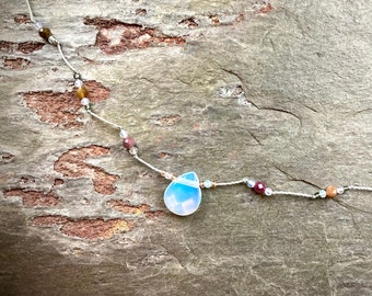 May include: A delicate necklace with a light blue teardrop pendant and small, colorful beads on a white cord.
