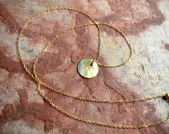 Può includere: Una collana con catena dorata e un ciondolo rotondo in metallo martellato iridescente.