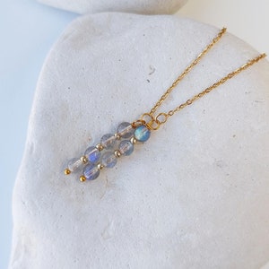 Op de afbeelding: Een gouden ketting met een hanger gemaakt van iriserende blauwe en grijze edelsteen kralen.