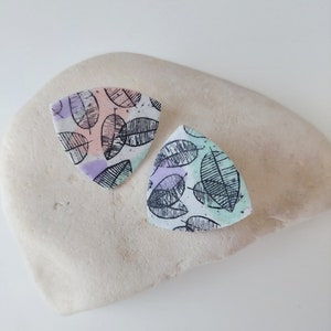 May include: A pair of triangular shaped earrings with a leaf pattern in black, pink, green, and purple.