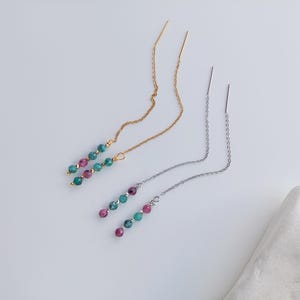 Op de afbeelding: Een paar oorringen met groene en roze edelsteen kralen aan een gouden en zilveren ketting.