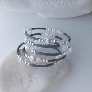 May include: A gray silicone bracelet with clear glass beads and silver beads. The bracelet is wrapped around itself multiple times.
