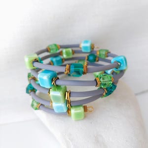 May include: A multi-layered bracelet with gray elastic bands and green and blue glass beads. The beads are square and rectangular in shape.