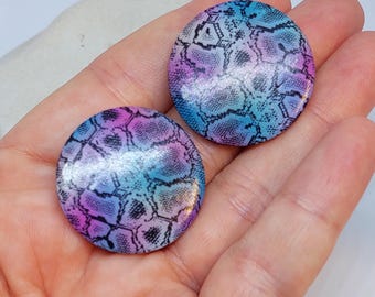 Peut inclure: Une paire de boucles d'oreilles rondes et colorées avec un motif de peau de serpent. Les boucles d'oreilles sont de couleur bleu clair, rose et violet avec des accents noirs.