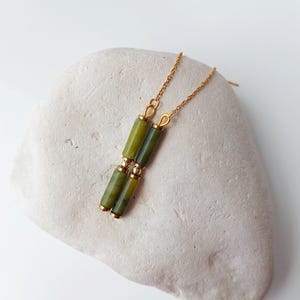 Op de afbeelding: Een paar gouden oorbellen met groene jade-steen accenten. De oorbellen zijn gemaakt van een delicate ketting met twee jade-stenen aan elke oorbel.