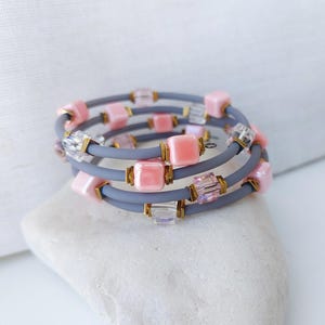 May include: A multi-layered bracelet with gray elastic bands and pink and clear square beads.