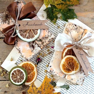 May include: A still life composition showcasing dried citrus slices, each with a "Handmade" tag, alongside brown ribbons, autumnal leaves, and vintage book pages. The scene evokes a rustic, seasonal feel, with a focus on natural elements.