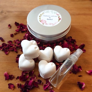 Peut inclure: Un ensemble de bombes de bain en forme de cœur blanc dans une boîte en étain argentée avec une étiquette qui indique "Handmade with love by Ismini". Les bombes de bain sont entourées de pétales de rose séchés.