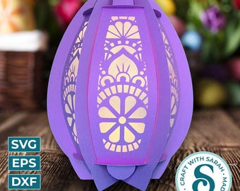 May include: Purple papercraft Easter egg lamp with a white intricate design. The lamp is made of multiple layers of paper and has a delicate, floral pattern. The lamp is lit from within, creating a warm glow.