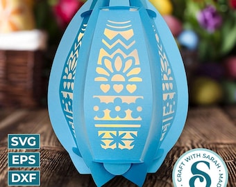 May include: A blue papercraft Easter egg lantern with intricate cut-out designs. The lantern has a white interior and a light source shining through the cut-outs.