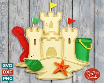 May include: A papercraft sandcastle with a red shovel, green bucket, yellow and green flags, a starfish, and a seashell. The sandcastle is on a wooden background with the text "Craft with Sarah".