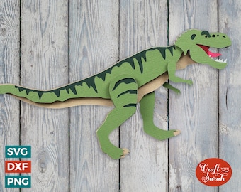 May include: Green papercraft dinosaur cutout against a woodgrain background. The dinosaur is in a walking pose with its mouth open and tongue sticking out. The text "Craft with Sarah" is in a red circle in the lower right corner of the image.