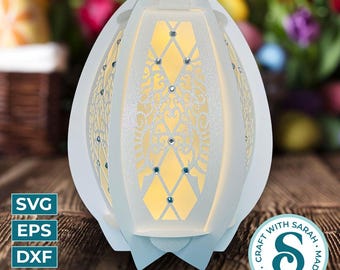 May include: A white, egg-shaped decorative lamp with intricate cut-out patterns and embedded rhinestones. The lamp has a soft, glowing interior. The design includes floral and geometric elements. The lamp is on a wooden surface.