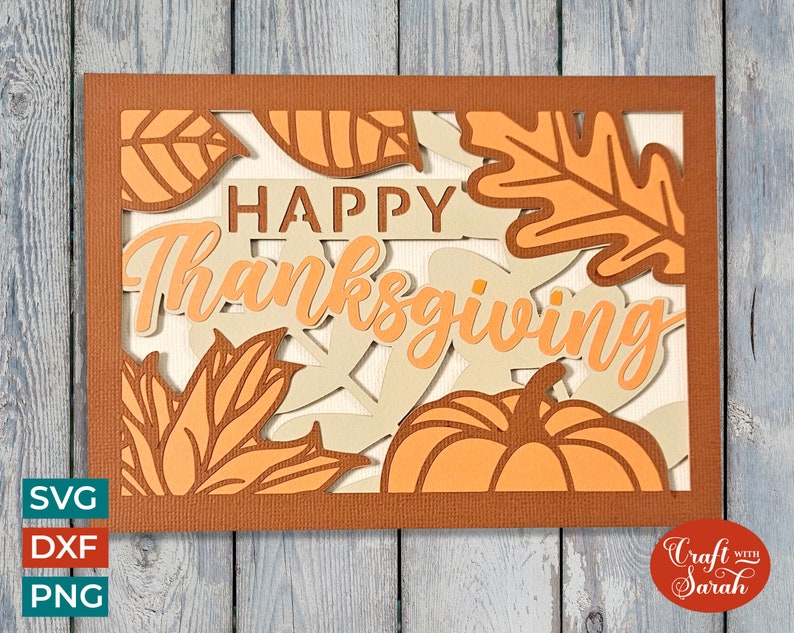 K&ouml;nnte beinhalten: Eine braune Karte mit einem Ausschnitt-Design mit den Worten "Happy Thanksgiving" umgeben von Bl&auml;ttern und einem K&uuml;rbis. Die Karte befindet sich auf einem Holz-Hintergrund.