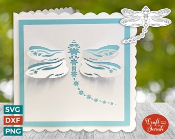 May include: A white card with a blue border and a white dragonfly cut out design. The dragonfly has a trail of stars behind it. The card has a scalloped edge and the words "Craft with Sarah" are printed on the bottom right corner.