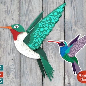 Puede incluir: Dos colibríes de papel recortados con intrincados patrones florales. El colibrí de la izquierda es verde, blanco y rojo. El colibrí de la derecha es morado, azul y verde. El fondo es una textura de madera.