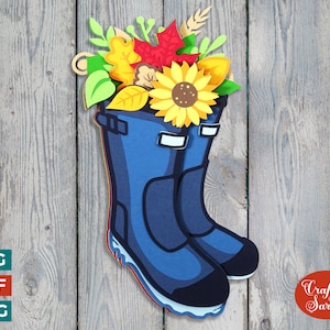 May include: Blue wellies with a bouquet of autumn leaves, sunflowers, and wheat stalks. The boots are on a wooden background.