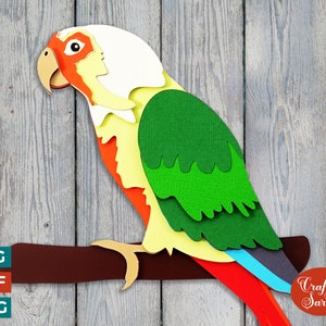 May include: Paper craft of a green, yellow, orange, and white parrot perched on a brown branch. The parrot is made of layered paper and has a detailed design. The image includes the text "Craft with Sarah".