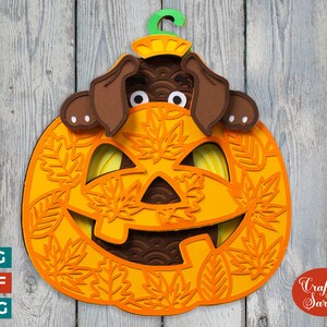 May include: A brown dog peeking out of an orange pumpkin with a carved jack-o'-lantern face. The pumpkin is decorated with orange and brown leaves. The text "Craft with Sarah" is in the lower right corner.