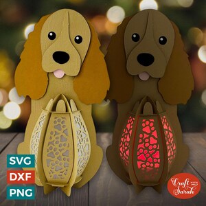 May include: Two brown and tan papercraft dog lanterns with a paw print design. The lanterns are lit with red and white lights. The lanterns are sitting on a wooden surface. Craft with Sarah.