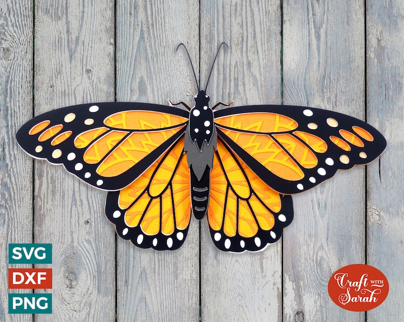 May include: A black and orange papercraft butterfly with intricate details. The butterfly is cut out and layered to create a 3D effect. The butterfly is against a wood background.