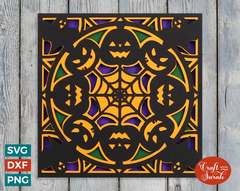 May include: A black square card with a Halloween-themed design. The design features a spiderweb in the center with jack-o'-lantern faces around the perimeter. The card is decorated with orange, green, and purple accents.