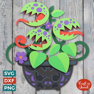 May include: A papercraft Halloween decoration featuring a three-headed carnivorous plant in a black pot with a bat and skull design. The plant has green leaves, red tongues, and purple spots.