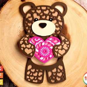 Könnte beinhalten: Brauner Teddybär, der ein pinkfarbenes Herz mit einem Wirbelmuster hält. Der Bär ist mit kleinen braunen Herzen bedeckt.