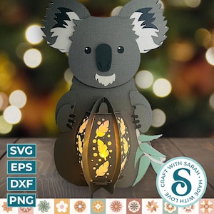 Könnte beinhalten: Ein grauer Koala hält eine Papierlaterne mit einem gelben Licht, das durchscheint. Die Laterne hat ein Muster aus Blättern und Punkten. Der Koala steht auf einer Holzoberfläche. Der Text "CRAFT WITH LOVE. MADE WITH SARAH." befindet sich in einem Kreis mit einem stilisierten "S" in der Mitte.