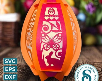 May include: A 3D papercraft Easter egg lantern with a pink and orange color scheme. The egg is decorated with a butterfly, bunny, and floral designs. The lantern is made to be assembled and lit from within.