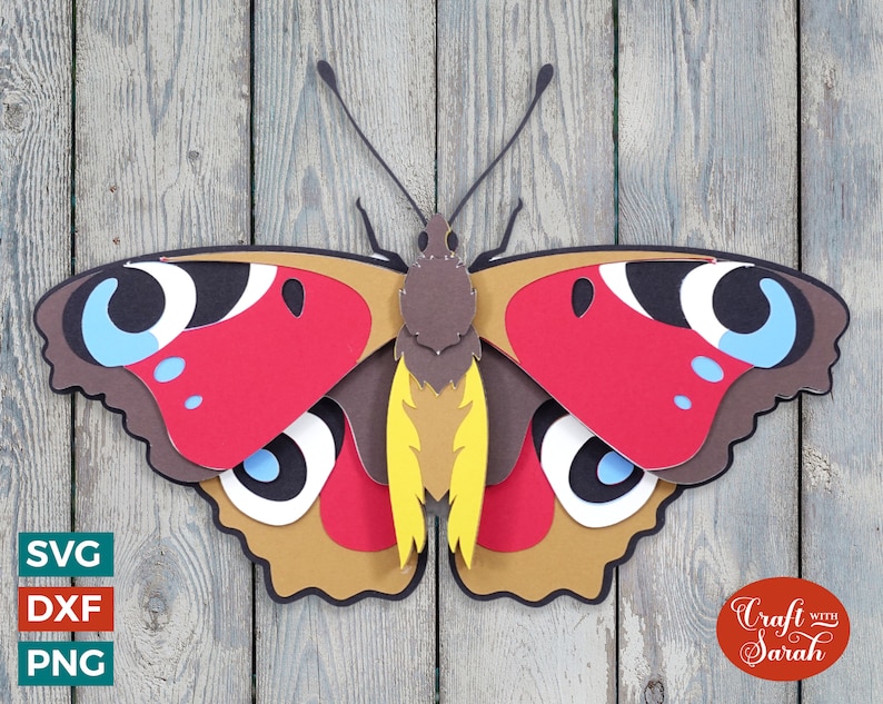 Może przedstawiać: Papierowy motyl z brązowymi, czerwonymi, ż&oacute;łtymi, niebieskimi i białymi skrzydłami. Motyl jest warstwowy i ma efekt 3D. Motyl znajduje się na tle drewnianym.