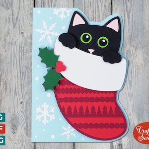 Peut inclure: Un chat noir aux yeux verts sort d'une chaussette de Noël rouge et blanche avec une branche de houx verte. La chaussette est sur un fond bleu avec des flocons de neige blancs.