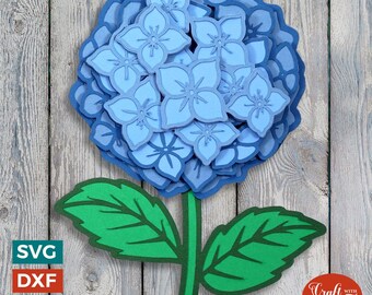 Peut inclure: Une fleur en papier bleue avec des feuilles vertes et une tige. La fleur est composée de nombreuses couches de fleurs en papier bleues. La fleur est sur un fond en bois.