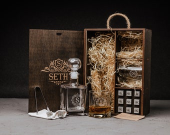 May include: A wooden box with a personalized engraved name "SETH" on the front. The box contains a glass decanter, two glasses, and a set of whiskey stones. The box is lined with straw.