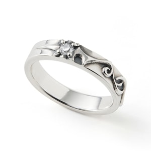 May include: A silver ring with a central clear gemstone and decorative scrollwork. The ring has a polished finish and a band that tapers slightly towards the back. The gemstone is set in a raised setting, adding a touch of elegance to the design.