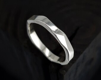 May include: A silver ring with a unique, faceted design. The ring has a geometric shape with multiple flat surfaces, creating a textured appearance. The band is approximately 0.25 inches wide, and the ring is set against a dark background.