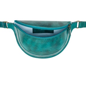 May include: A teal blue leather fanny pack with a zipper closure and a gold buckle. The bag is open and the inside is lined with a light blue fabric.