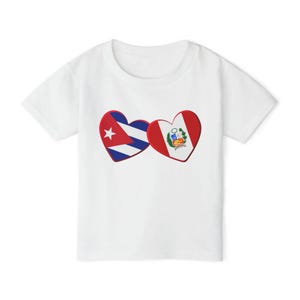 Könnte beinhalten: Ein weißes T-Shirt mit kurzen Ärmeln und einer Grafik von zwei herzförmigen Flaggen nebeneinander. Das linke Herz zeigt die kubanische Flagge mit ihren blauen und weißen Streifen, einem roten Dreieck und einem weißen Stern.