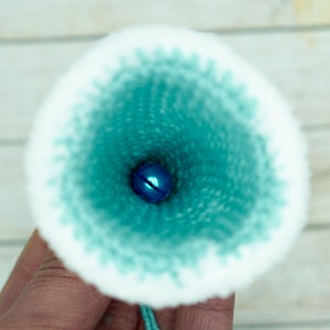 K&ouml;nnte beinhalten: Nahaufnahme des Inneren eines tealblauen, gestrickten Stoffkegels mit einer kleinen blauen Glocke am Boden.