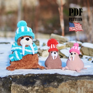 May include: Three crocheted walrus figures wearing winter hats and scarves. The largest walrus is brown with a blue and white hat and scarf. The other two are smaller, one brown with a red hat, and one pink with a pink and white hat. The image includes the text "PDF PATTERN".