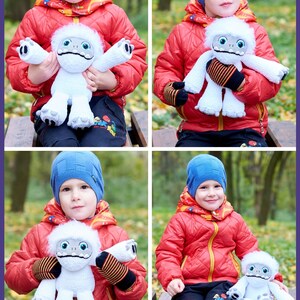 May include: A young person wearing a red jacket and blue hat is holding a white plush toy with a black nose and eyes. The toy is a Yeti from the movie "Abominable".