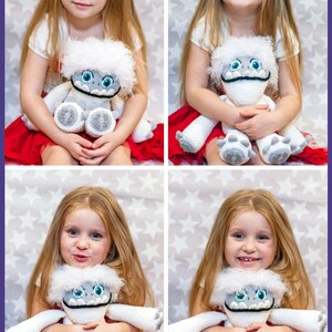 May include: A young girl is holding a white crocheted Yeti plush toy with blue eyes and a black mouth. The toy has a white fur trim around its head and arms. The girl is wearing a red skirt and has long blonde hair. The background is a white surface with silver stars.
