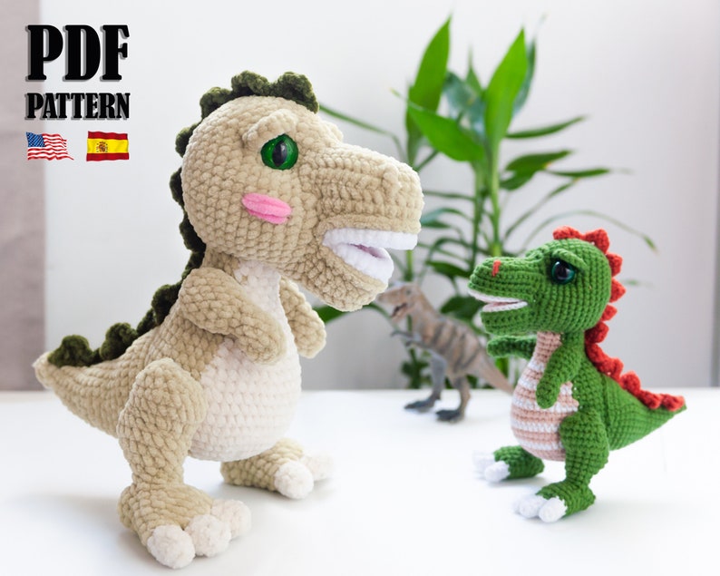 May include: Two crocheted dinosaur toys. The larger dinosaur is beige with green accents and has a pink blush on its cheeks. The smaller dinosaur is green with red accents. Both dinosaurs have large, black eyes.