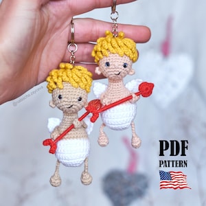 Puede incluir: Dos llaveros de Cupido hechos a mano con ganchillo. Cada Cupido tiene cabello amarillo, alas blancas y una flecha roja. Los llaveros están sujetos a anillos plateados. La imagen también incluye el texto "PDF PATTERN" y una pequeña bandera estadounidense.