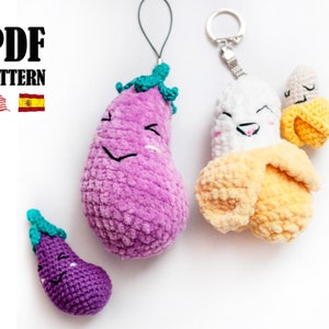 Puede incluir: Tres juguetes de peluche de crochet: una berenjena morada, un plátano amarillo y una berenjena morada más pequeña. La banana y la berenjena más grande tienen caras sonrientes y están unidas a llaveros. La berenjena más pequeña es un llavero.