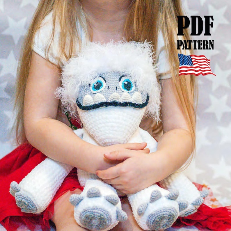 May include: A crocheted white yeti plush toy with blue eyes and a black mouth. The yeti is sitting in the lap of a child wearing a red dress.