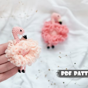 May include: Two pink crocheted flamingo amigurumi toys. The smaller flamingo is standing on a white surface. The larger flamingo is being held in a person's hand. The text "PDF PATTERN" is visible at the bottom of the image.