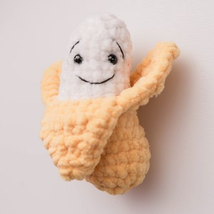 May include: A crocheted banana plush toy with a smiling face. The banana is white with a yellow peel.