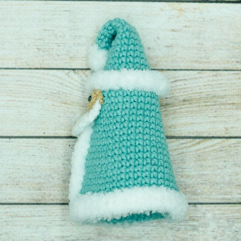 K&ouml;nnte beinhalten: Ein geh&auml;kelter, t&uuml;rkisfarbener Weihnachtsmann-Anh&auml;nger mit wei&szlig;em Pelzbesatz und einem wei&szlig;en Bommel auf der M&uuml;tze.